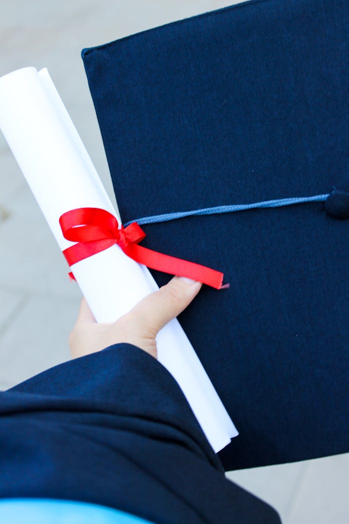 Close-up of a hand holding a diploma and graduation cap, symbolizing achievement.